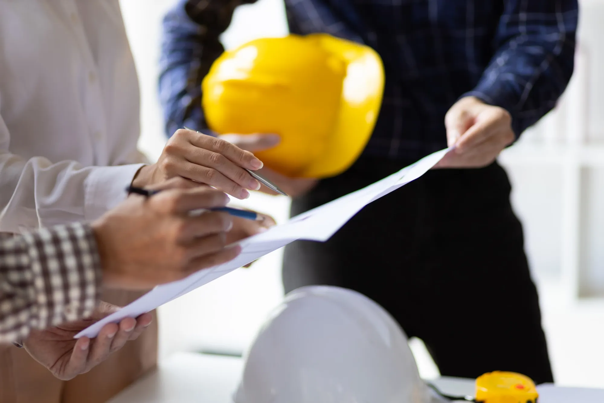 Hands reviewing technical documents next to a yellow hard hat